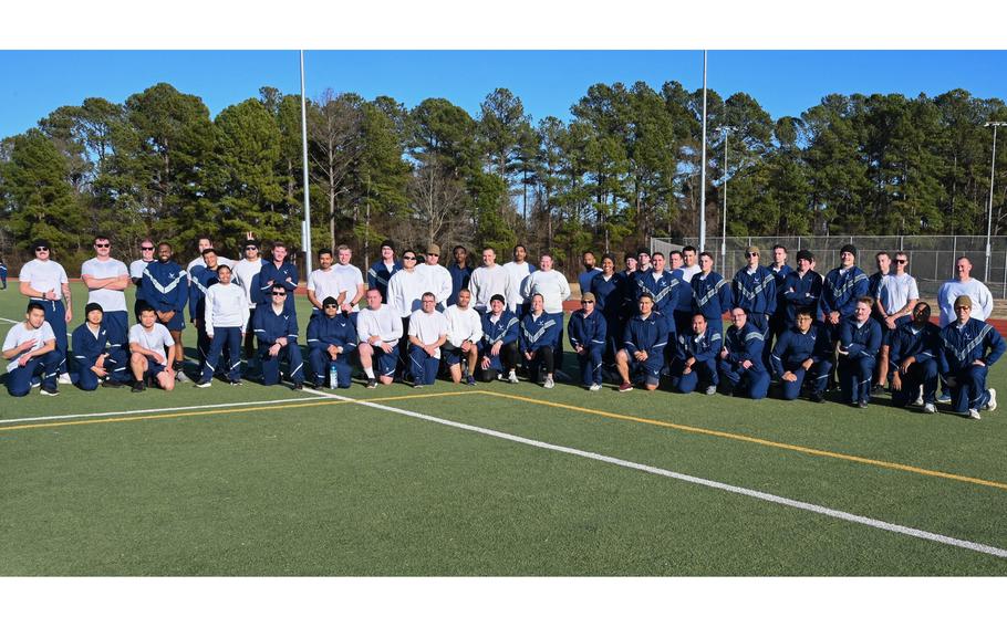 Airmen in workout clothing pose for a photo on a grass field.
